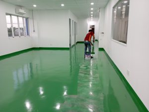 Thi Công Sơn Sàn Epoxy Nhà Xưởng Tại KCN VSIP 2A Tân Uyên Chuẩn bị bề mặt: Bề mặt sàn cần được làm sạch hoàn toàn để loại bỏ bụi, dầu mỡ, hạt cát và các tạp chất khác. Cần sử dụng các phương pháp như đánh bóng, cắt, mài hoặc xử lý hóa chất để đảm bảo bề mặt mịn và sạch. Sửa chữa bề mặt: Nếu có các vết nứt, lỗ hoặc bất kỳ hỏng hóc nào trên bề mặt sàn, chúng cần được sửa chữa trước khi tiến hành thi công sơn epoxy. Việc này đảm bảo rằng bề mặt sẽ đồng đều và không có vấn đề gì ẩn. Áp dụng lớp sơn epoxy: Sau khi bề mặt được chuẩn bị, lớp sơn epoxy sẽ được áp dụng bằng cách sử dụng các công cụ như cuộn sơn, cọ, bàn chải hoặc máy phun sơn. Cần chú ý đến việc đảm bảo lớp sơn được phủ đều và không để lại vết lỡ. Phủ lớp phủ bảo vệ (nếu cần): Đối với môi trường có mức độ tải trọng cao hoặc tiếp xúc với hóa chất, có thể cần áp dụng thêm một lớp phủ bảo vệ sau khi lớp sơn epoxy đã khô. Thời gian khô và chuẩn bị sử dụng: Lớp sơn epoxy cần có thời gian để khô hoàn toàn trước khi bàn giao sàn để sử dụng. Thời gian khô thường phụ thuộc vào điều kiện thời tiết và loại sơn được sử dụng. Bảo trì và vệ sinh: Sau khi sàn đã được hoàn thành, cần duy trì và vệ sinh thường xuyên để đảm bảo tuổi thọ và độ bóng của lớp sơn epoxy. Quá trình thi công sơn sàn epoxy cần có sự chuyên nghiệp và kỹ thuật, nên thường được thực hiện bởi các công ty chuyên nghiệp trong lĩnh vực xây dựng và hoàn thiện nhà xưởng.